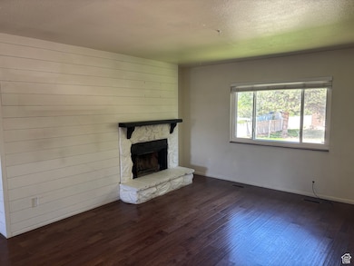 Unfurnished living room with wood finished floors, a stone fireplace, and a textured ceiling