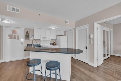 Kitchen with white appliances, a breakfast bar, wood finished floors, and dark countertops