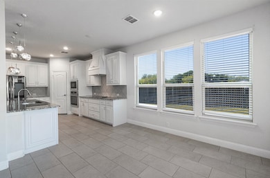Kitchen with white cabinetry, dark stone countertops, backsplash, pendant lighting, and stainless steel appliances