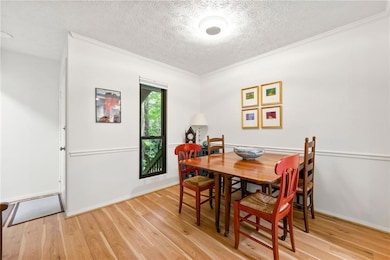 Dining area with light wood-style floors, a textured ceiling, and crown molding