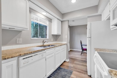 Kitchen with white cabinetry, sink, white appliances, and light hardwood / wood-style flooring