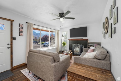 Living area with a fireplace, dark wood-type flooring, a textured ceiling, and a ceiling fan