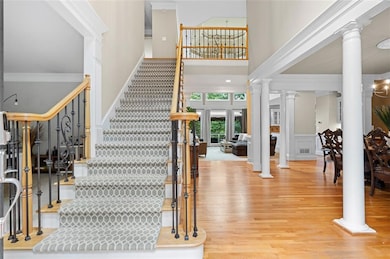 Staircase featuring decorative columns, a high ceiling, wood finished floors, crown molding, and wainscoting