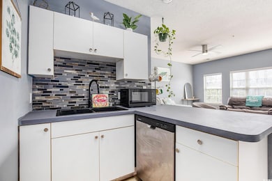 Kitchen with dishwasher, a sink, black microwave, a peninsula, and tasteful backsplash