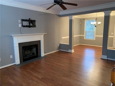 Unfurnished living room with crown molding, wood finished floors, a ceiling fan, a fireplace with flush hearth, and a chandelier