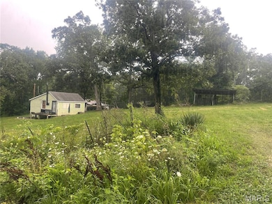 View of green lawn with a carport and a wooded view