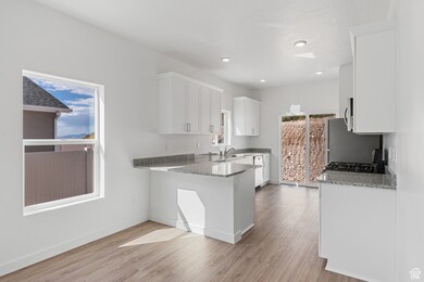 Kitchen with light stone countertops, white cabinetry, a peninsula, light wood-type flooring, and recessed lighting