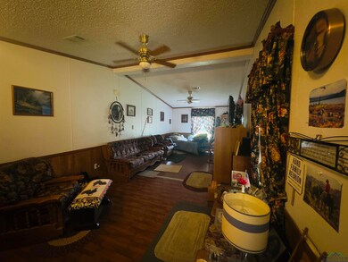 Living area featuring a ceiling fan, a textured ceiling, ornamental molding, and wood finished floors
