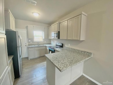 Kitchen featuring appliances with stainless steel finishes, a peninsula, light stone countertops, and wood finish floors