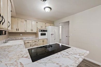 Kitchen featuring light countertops, white appliances, dark wood-type flooring, and light brown cabinets
