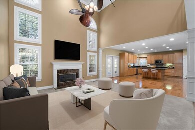 Two story grand room area with decorative columns, a high ceiling, healthy amount of natural light, a fireplace, and light wood-style flooring
