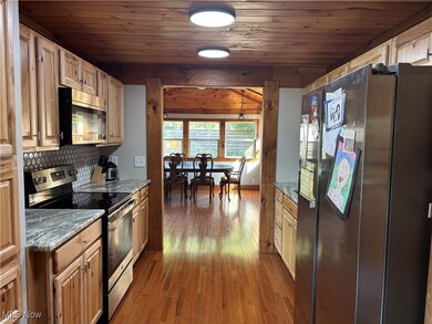 Kitchen featuring stainless steel appliances, dark wood-style flooring, light stone counters, wood ceiling, and backsplash