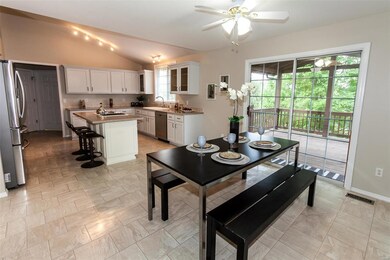 Kitchen/breakfast room with vaulted ceiling, white cabinets, solid surface counter top, breakfast bar, planning desk and stainless steel appliances. Sliding door leads to covered deck, concrete patio and tree lined backyard.