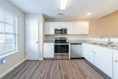 Kitchen featuring visible vents, wood finished floors, stainless steel appliances, white cabinetry, and a sink