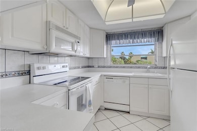 Kitchen featuring white appliances, white cabinetry, light countertops, decorative backsplash, and light tile patterned floors