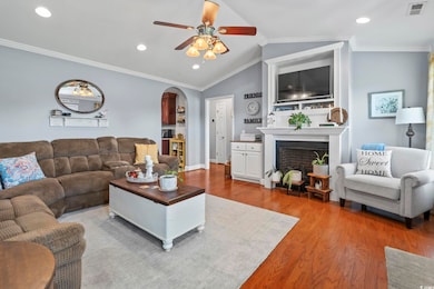Living room with wood finished floors, a ceiling fan, vaulted ceiling, arched walkways, and a fireplace