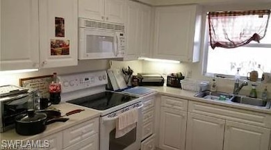 Kitchen with a sink, white appliances, and white c