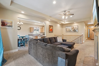 Living room featuring a tray ceiling, light carpet, recessed lighting, ceiling fan, and a chandelier