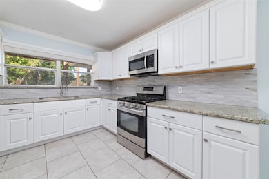 Fully renovated kitchen with crisp white cabinetry, quartz counters, and stainless steel appliances. Note the beautiful tile backsplash, gas cooktop and OTR microwave, coupled with large double stainless steel sink with industrial sprayer faucet.