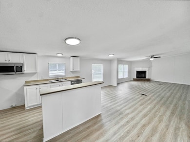 Kitchen featuring appliances with stainless steel finishes, a textured ceiling, white cabinets, light wood-style floors, and a fireplace with raised hearth