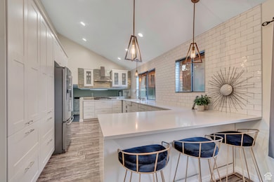 Kitchen featuring glass insert cabinets, a breakfast bar, vaulted ceiling, a peninsula, and white cabinets