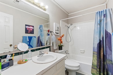 Full bathroom featuring shower / bath combination with curtain, ornamental molding, vanity, and a textured wall
