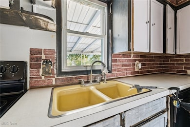 Kitchen with light countertops, black range, decorative backsplash, and white cabinets