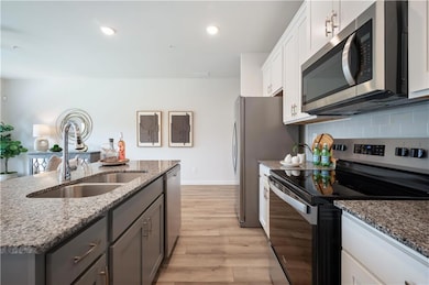 Kitchen with appliances with stainless steel finishes, light stone countertops, light wood-type flooring, recessed lighting, and white cabinetry