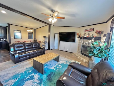 Carpeted living room featuring ornamental molding, a fireplace, ceiling fan, and lofted ceiling