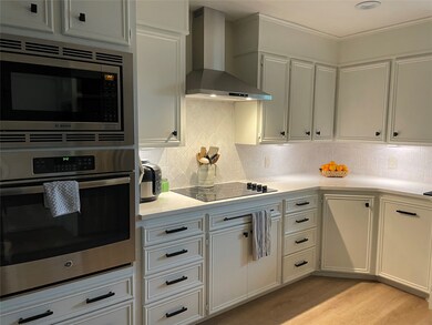 Kitchen featuring stainless steel appliances, wall chimney exhaust hood, light wood-style floors, tasteful backsplash, and light stone countertops