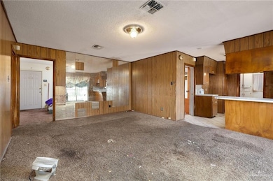 Unfurnished living room featuring wood walls, light carpet, and a textured ceiling