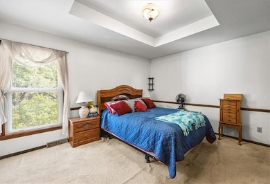 Carpeted bedroom featuring a tray ceiling and baseboards