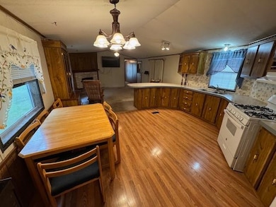 Kitchen with brown cabinetry, white range with gas cooktop, a peninsula, hanging light fixtures, and a chandelier