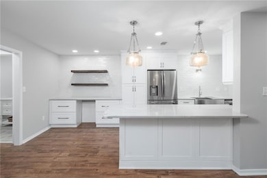 Kitchen with open shelves, white cabinetry, a peninsula, light stone counters, and decorative backsplash
