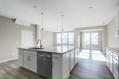 Kitchen with stainless steel dishwasher, light stone counters, pendant lighting, a kitchen island with sink, and white cabinetry