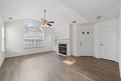 Unfurnished living room with ceiling fan, wood finished floors, a textured ceiling, a tiled fireplace, and lofted ceiling