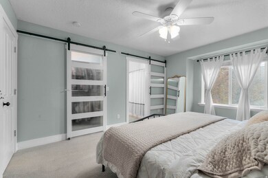Carpeted bedroom with a textured ceiling, a barn door, connected bathroom, and ceiling fan