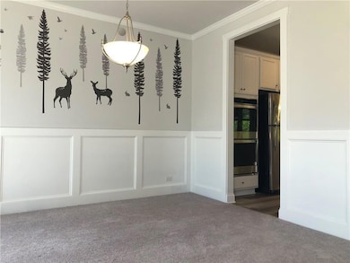Unfurnished dining area with a decorative wall, a wainscoted wall, crown molding, and carpet flooring