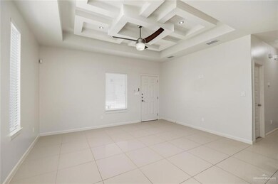 Empty room with coffered ceiling, a high ceiling, ceiling fan, and light tile patterned flooring