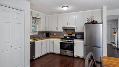 Kitchen with appliances with stainless steel finishes, decorative backsplash, dark wood-style flooring, white cabinetry, and a textured ceiling