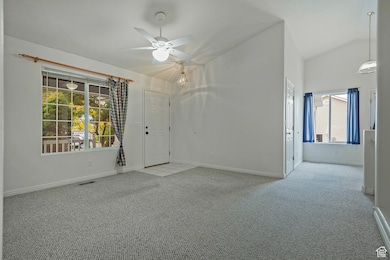 Empty room featuring light carpet, ceiling fan, and high vaulted ceiling