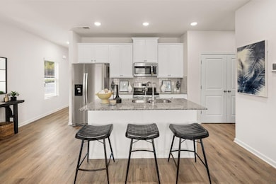 Kitchen featuring stainless steel appliances, a breakfast bar, a center island with sink, white cabinetry, and tasteful backsplash
