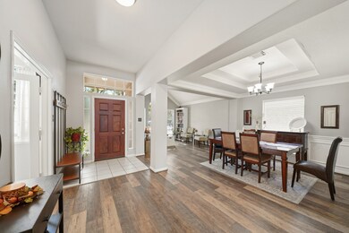 From this angle, you get a better view of the formal areas, gracefully divided by a soft, rounded column. Beautiful vinyl plank flooring flows seamlessly through the rooms, enhancing the open feel. The front door features decorative frosted sidelights on each side for added privacy, while multiple large windows fill the space with abundant natural light.