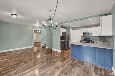 Kitchen with decorative backsplash, white cabinets, a peninsula, appliances with stainless steel finishes, and pendant lighting