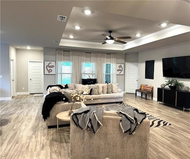Living room with crown molding, a tray ceiling, light wood finished floors, ceiling fan, and recessed lighting