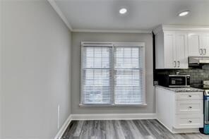 Kitchen featuring range hood, white cabinetry, baseboards, stainless steel microwave, and recessed lighting