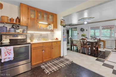 Kitchen with electric stove, brown cabinets, light countertops, a baseboard heating unit, and glass insert cabinets