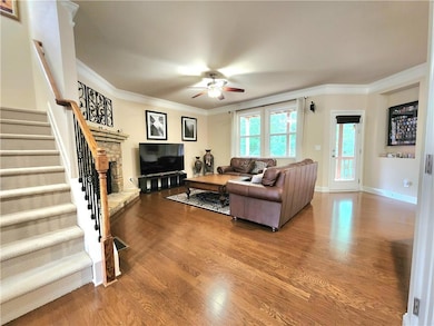 Living area featuring a ceiling fan, wood finished floors, stairway, ornamental molding, and a fireplace