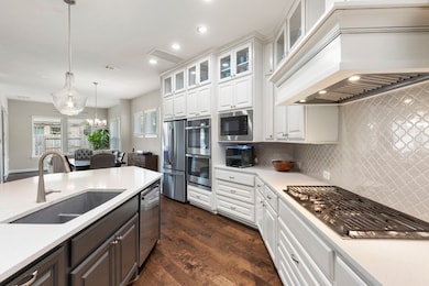 Elegant ceiling-height Shaker cabinetry with glass-front display uppers adds light and designer appeal to this stunning kitchen. Thoughtful details include  pots-and-pans drawers, double ovens, and a stylish backsplash.