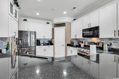 Kitchen with stainless steel appliances, tasteful backsplash, dark stone countertops, white cabinets, and ornamental molding